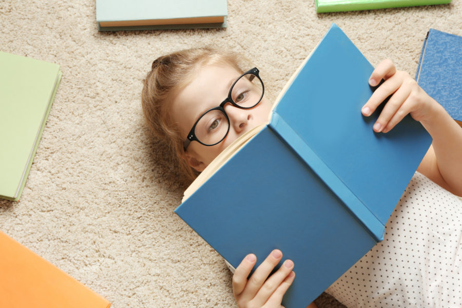 Cute,Little,Girl,Reading,Book,While,Lying,On,Carpet