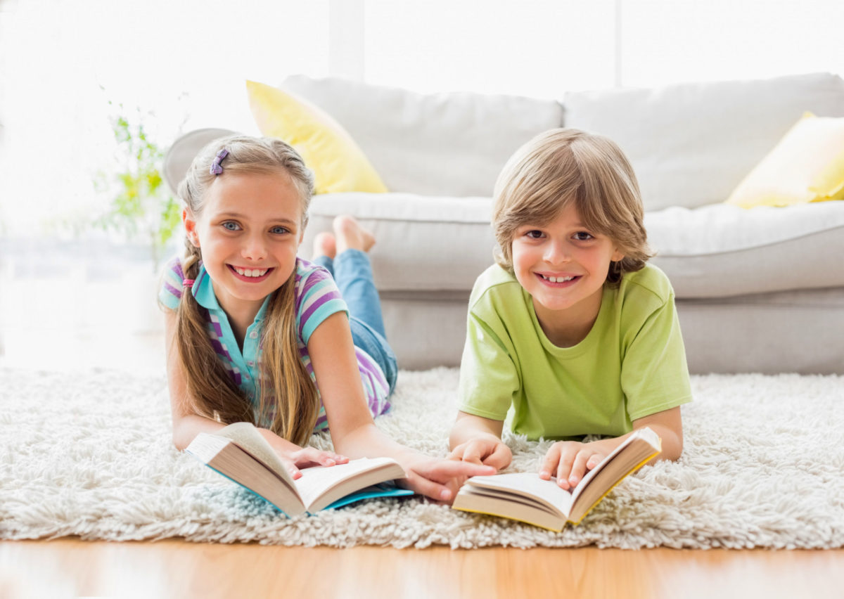 Happy siblings holding books while lying on rug
