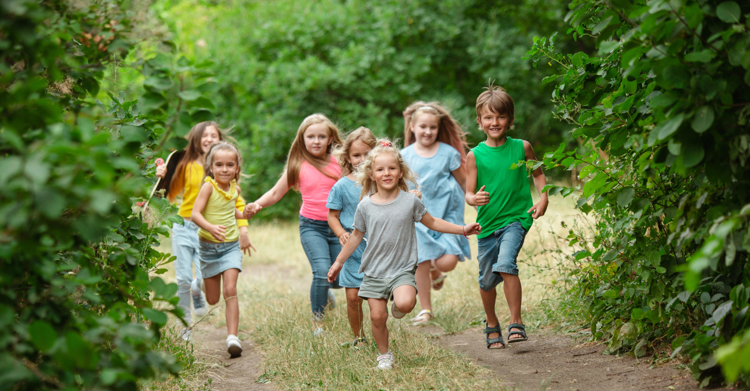 Kids, children running on green forest. Cheerful and happy boys and girs playing, laughting, running through green blooming meadow. Childhood and summertime, sincere emotions concept.